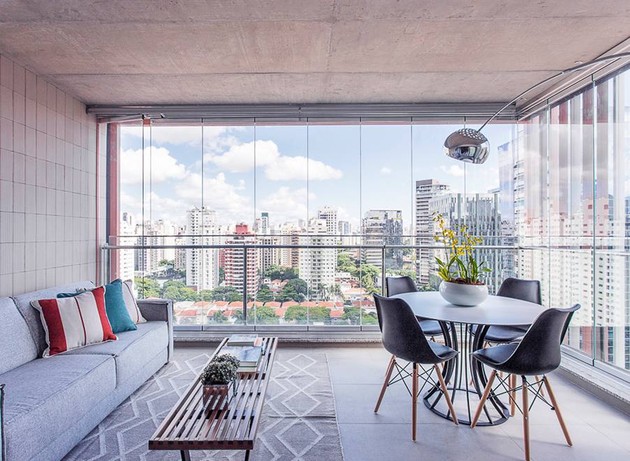 Terraço, varanda gourmet no Bairro do Itaim em São Paulo com tons de cinza de cimento queimado na composição um sofá confortável mesclado com uma mesa redonda e luminária de chão contemporânea. Projeto Andrade Shiki Design de Interiores